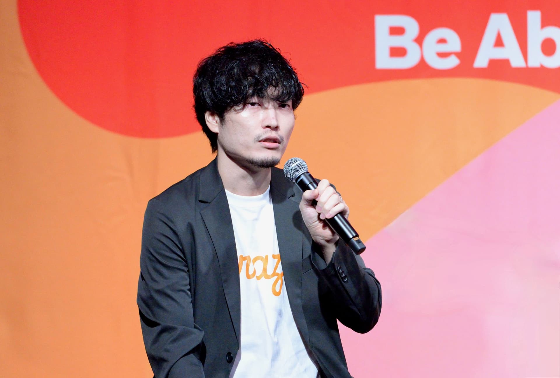 a man in a suit is holding a microphone in front of a pink and orange background .