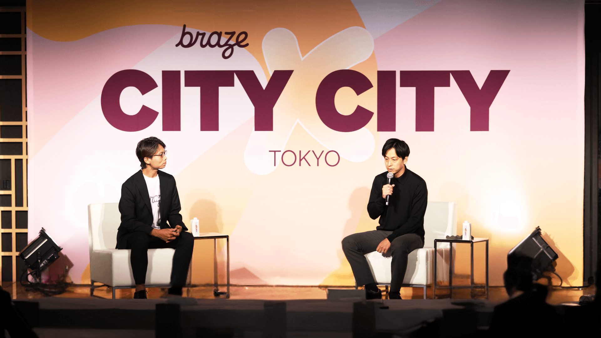two men sit in front of a sign that says braze city city tokyo