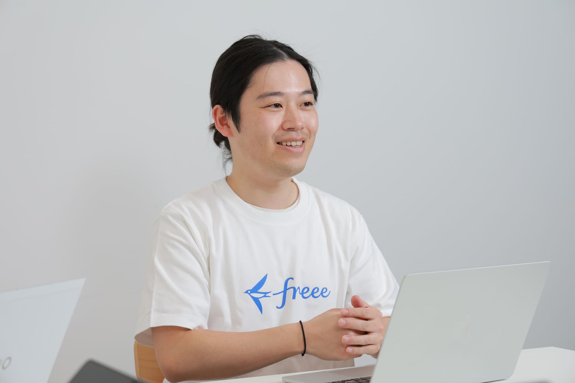 スモールビジネスプロダクト本部 個人プロダクト部 freee会計 プロダクトマネージャー 三船 大制氏がPCの前で手を組み話している。freeeのロゴTシャツを着ている