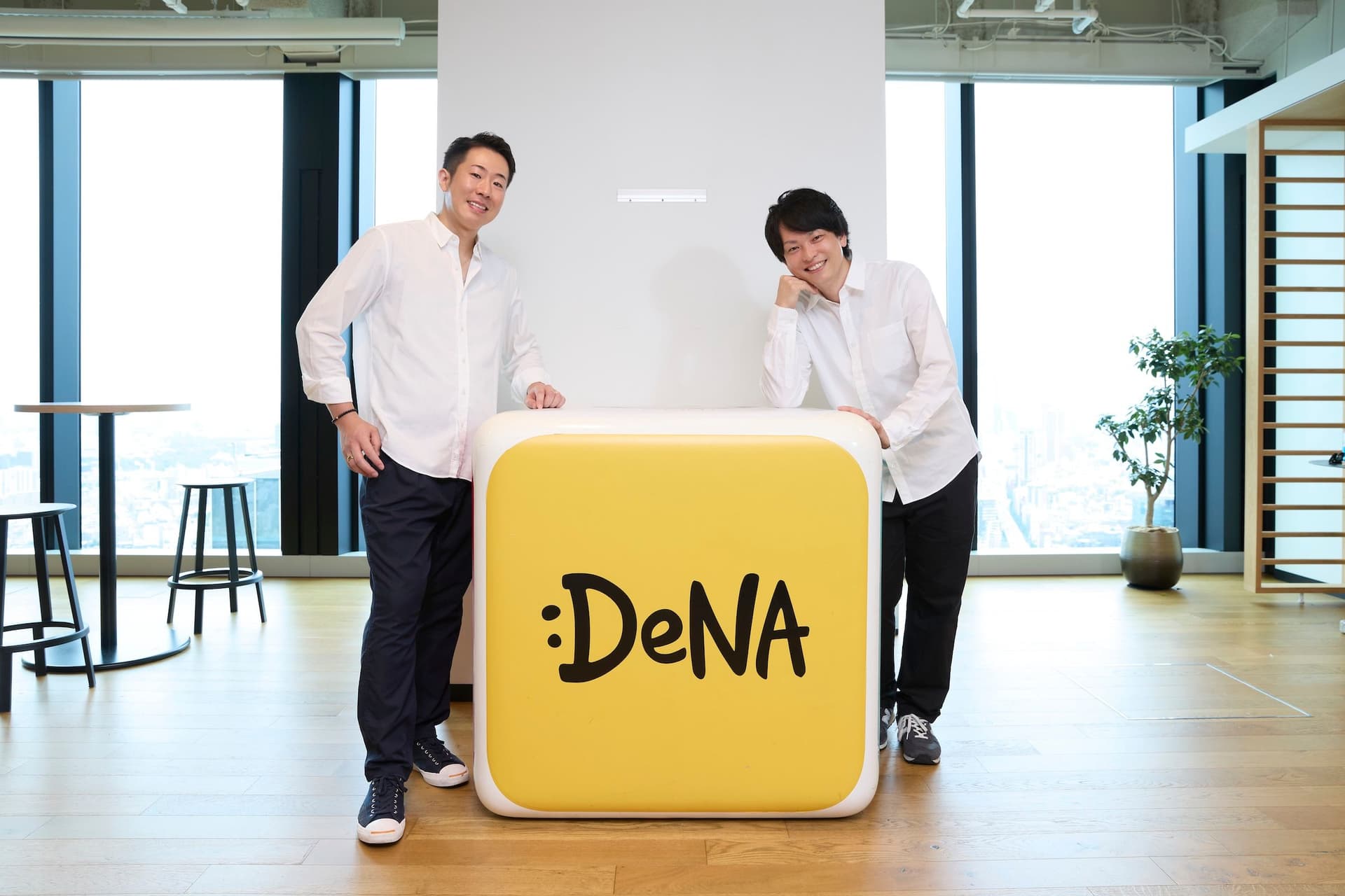 two men are standing next to each other in front of a dena logo .