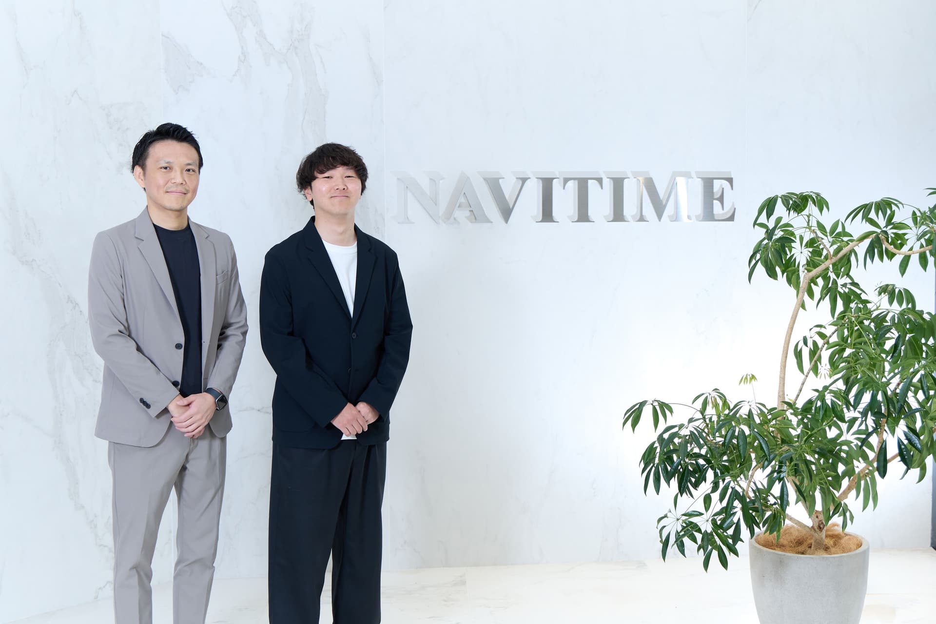 two men in suits are standing next to each other in front of a sign .
