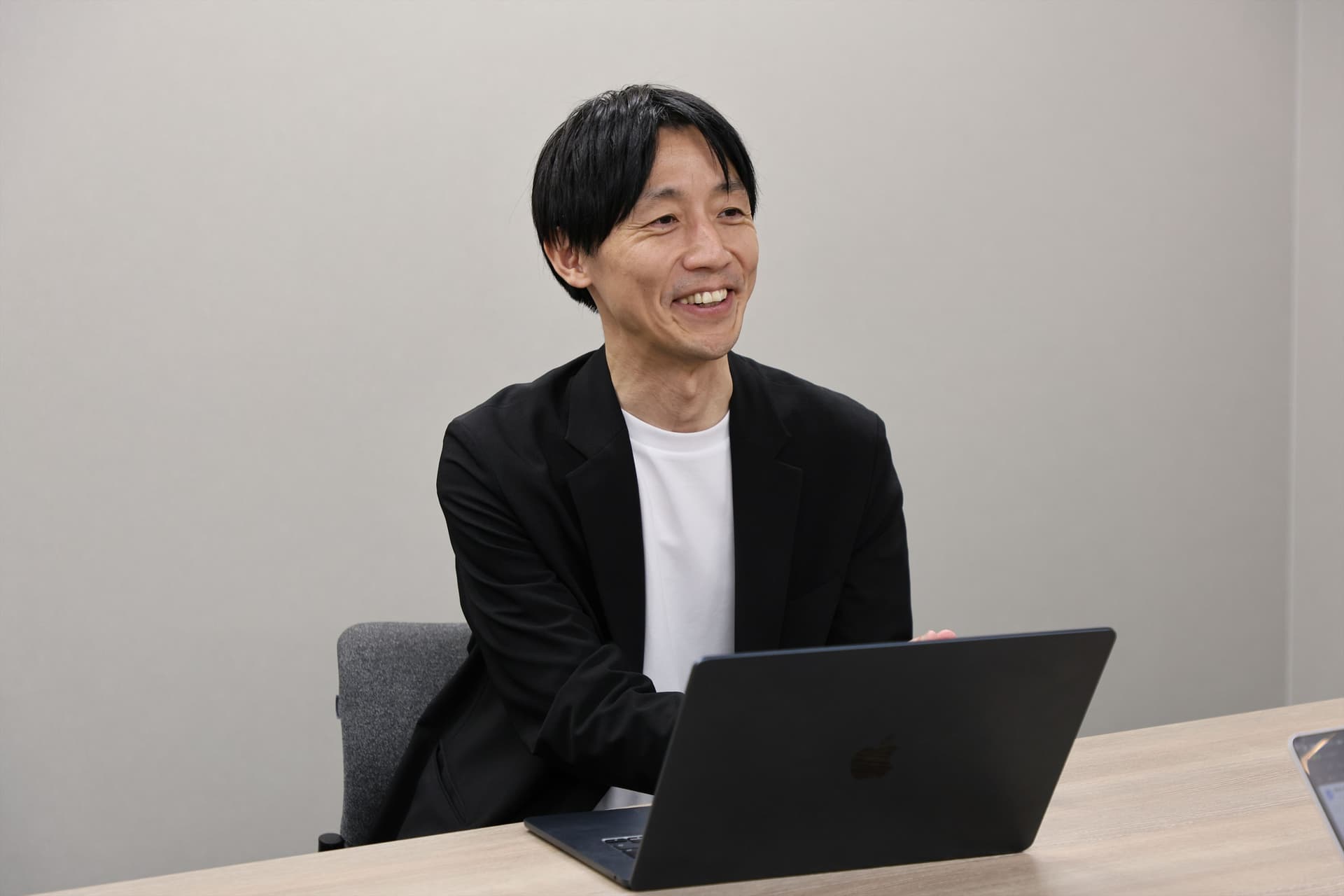 サツドラホールディングス株式会社 CDO兼株式会社サッポロドラッグストアー OMO本部本部長兼マーケティング部ゼネラルマネージャーの坂本 武史さんがインタビューを受けている様子。PCを前に笑顔で話をしている