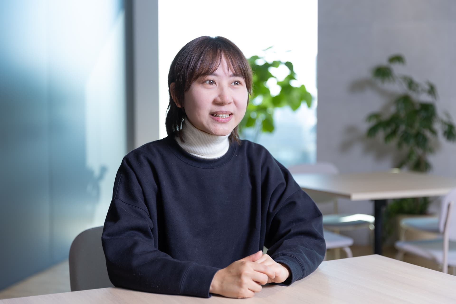 a woman is sitting at a table with her hands folded and smiling .