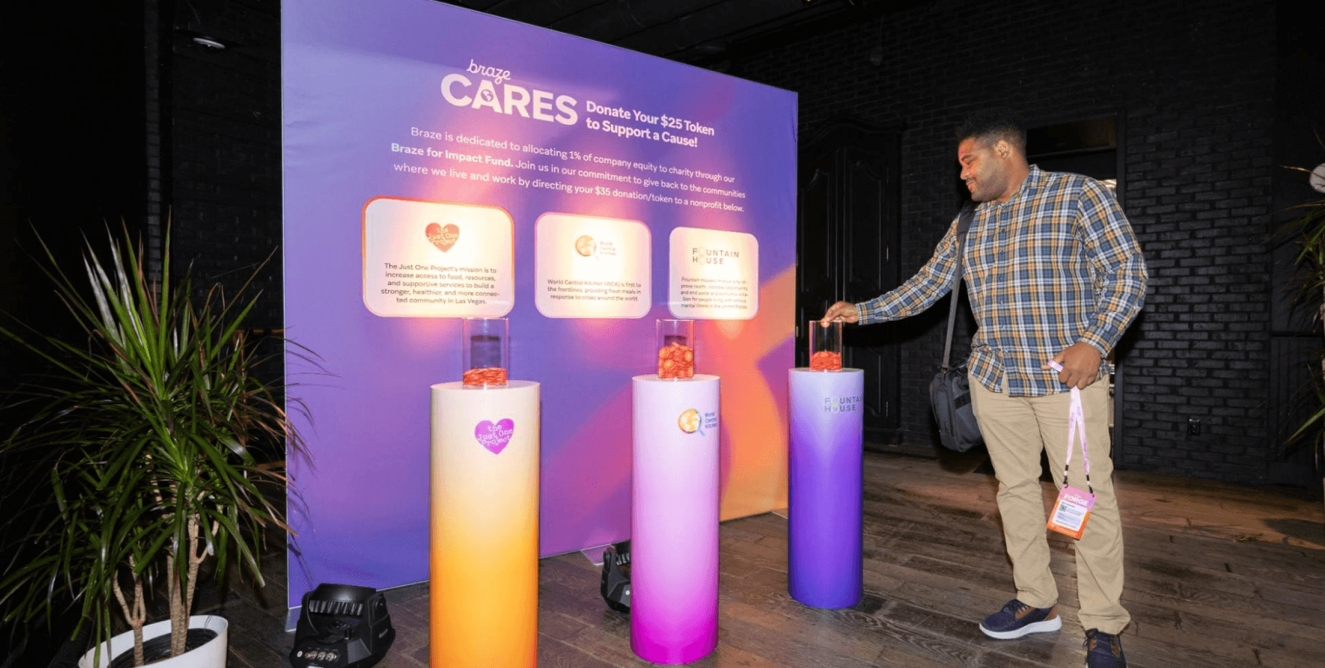 A man donates an orange token into one of three glowing bins at a Braze CARES charity display.