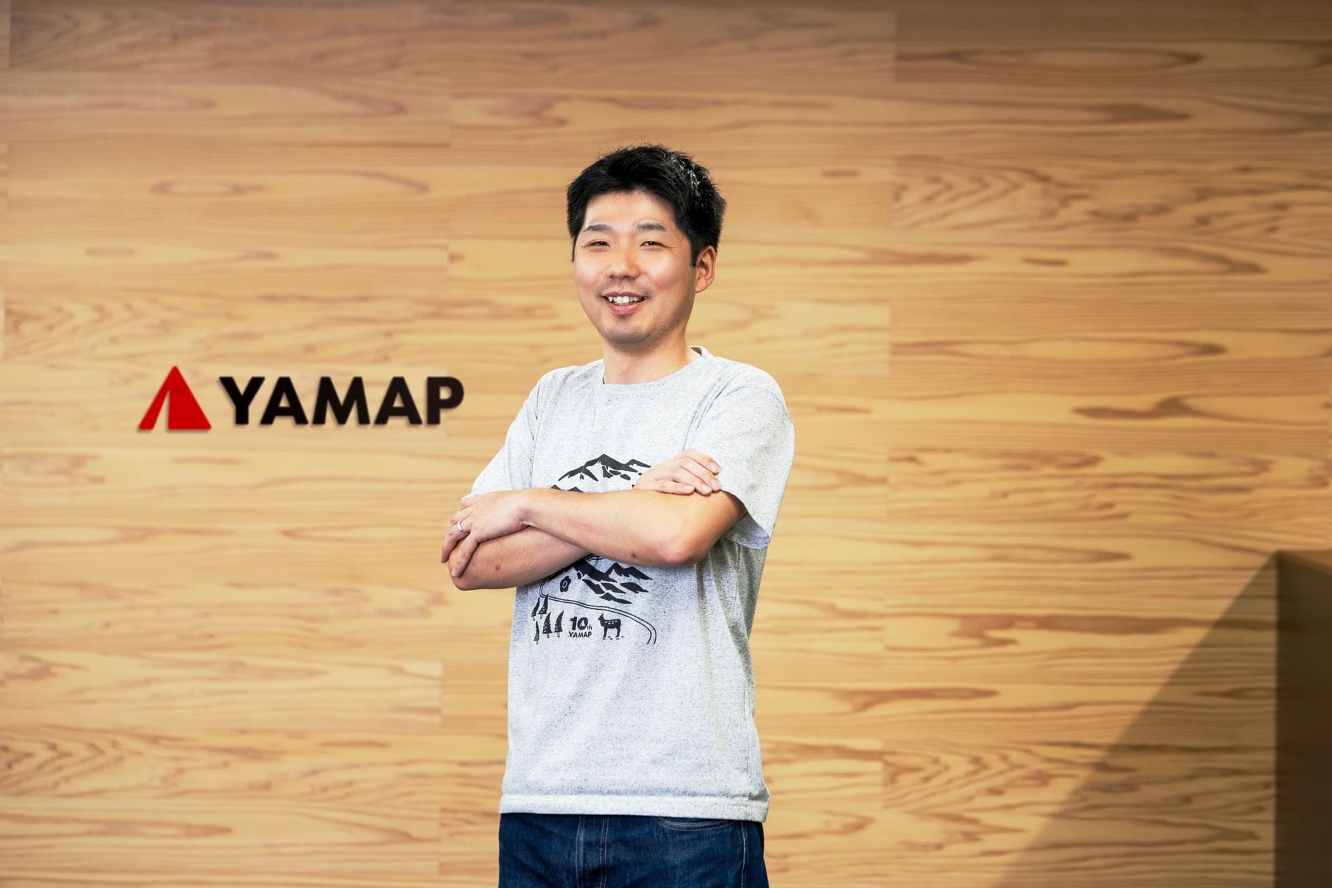 a man is standing in front of a wooden wall with his arms crossed .