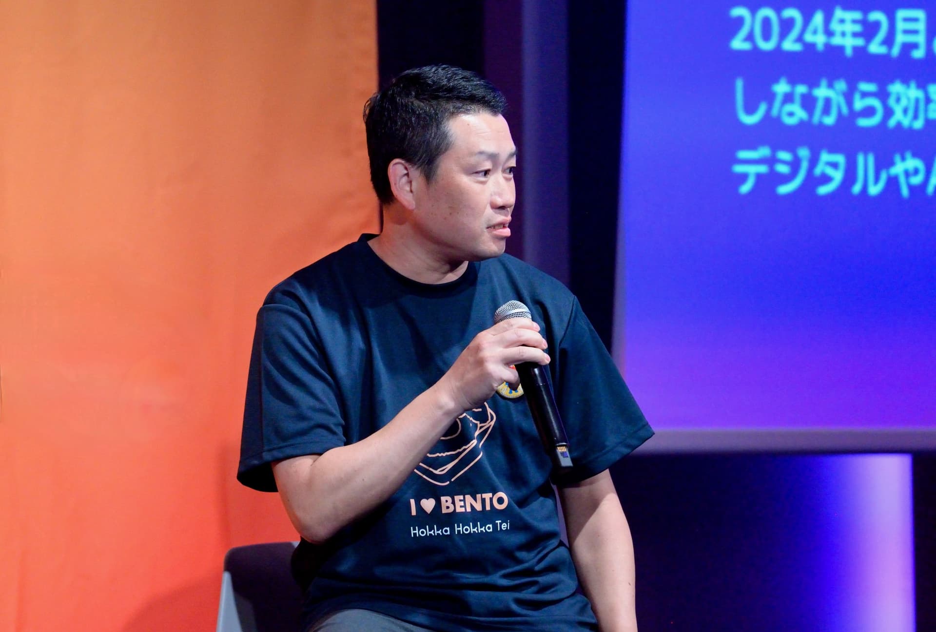 a man is sitting on a stage holding a microphone .