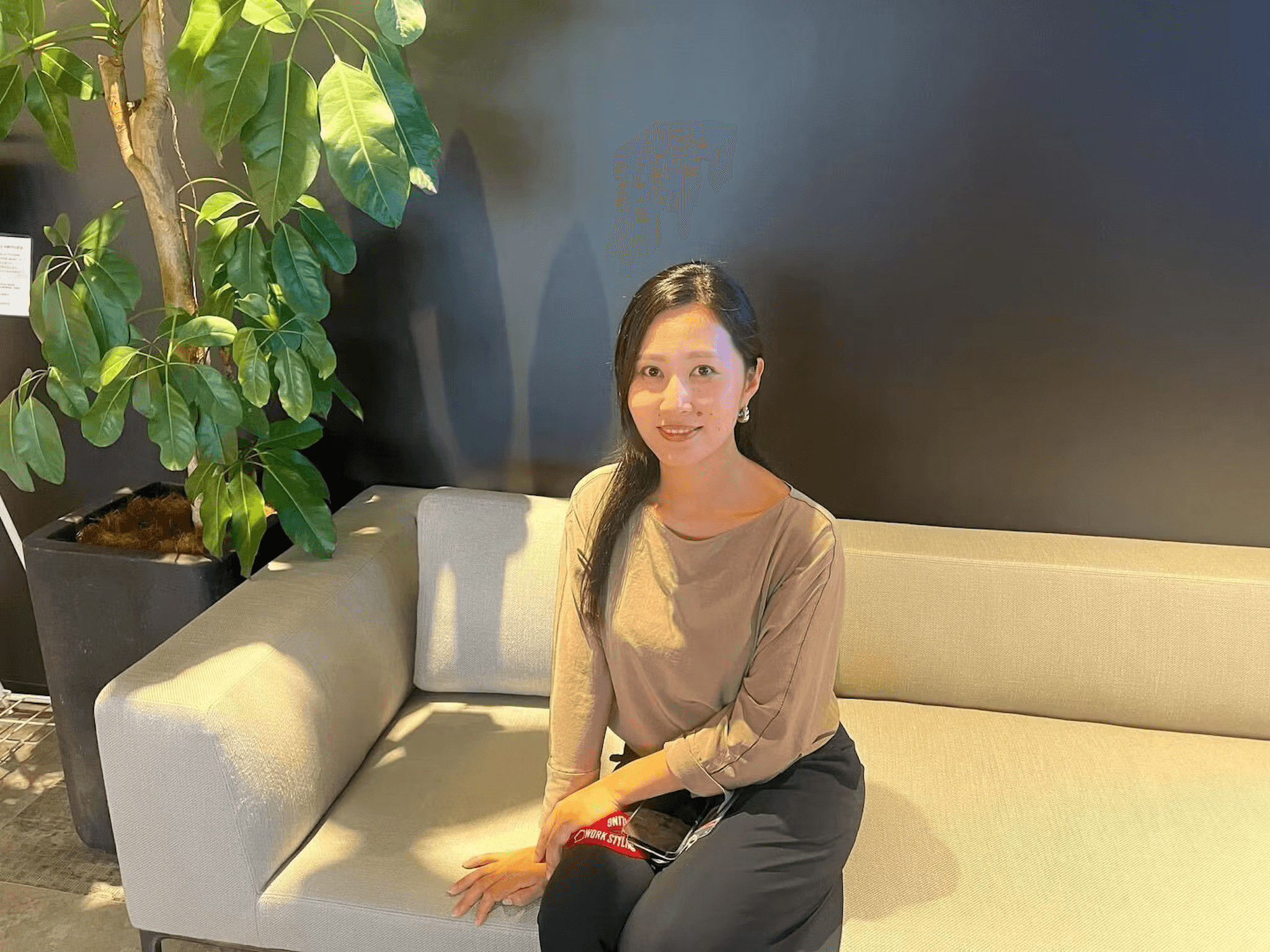 a woman sits on a couch with a plant in the background