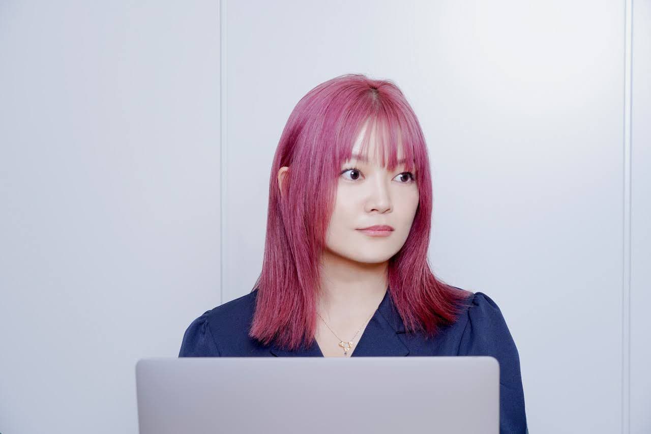 a woman with pink hair is sitting in front of a laptop computer .