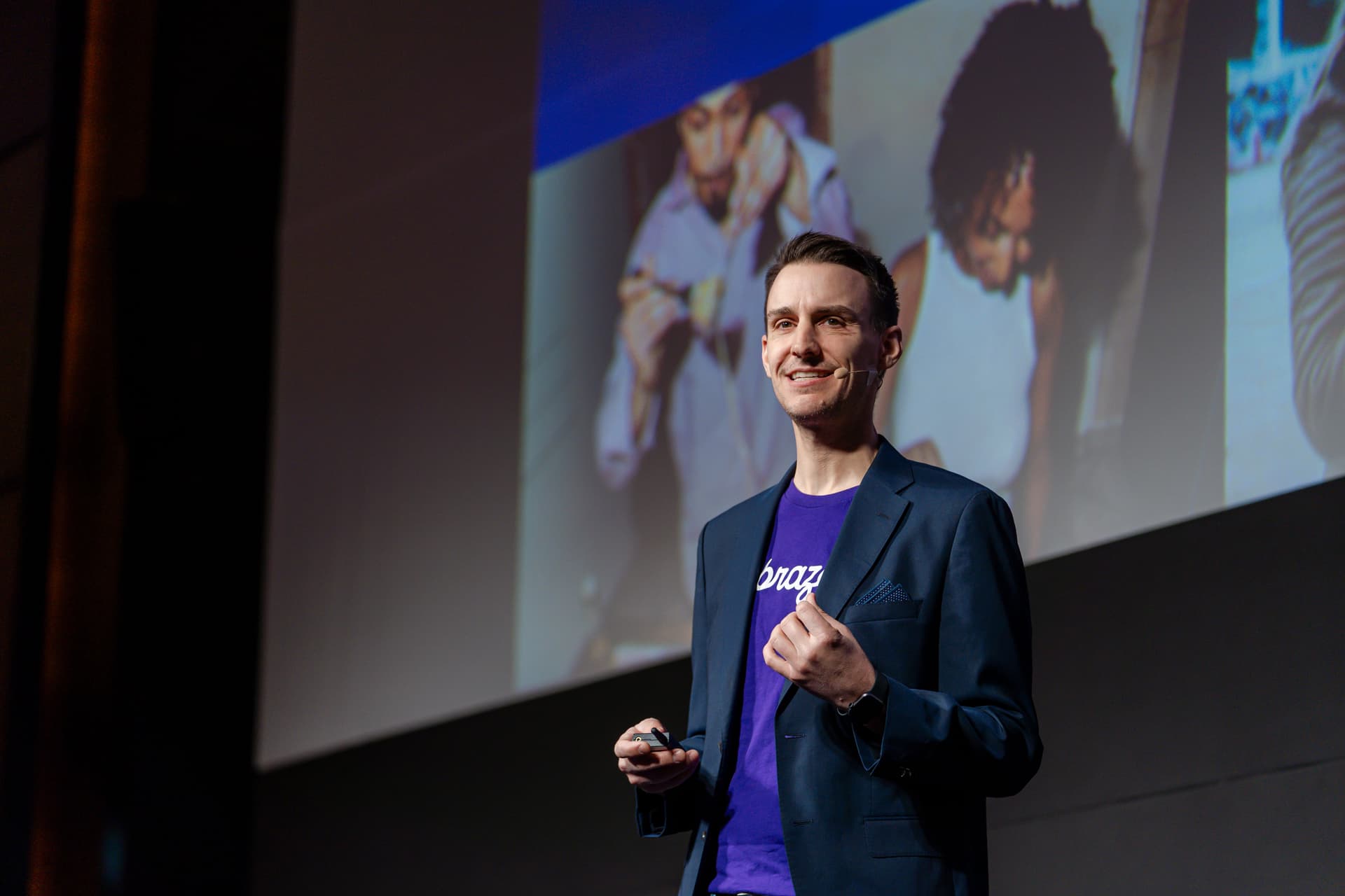 a man in a suit and purple shirt is giving a speech on a stage .