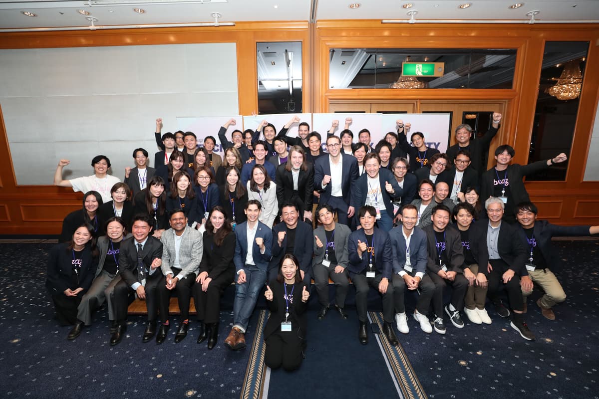 A large group of smiling, professionally dressed people, many raising their fists in celebration, in an indoor setting.