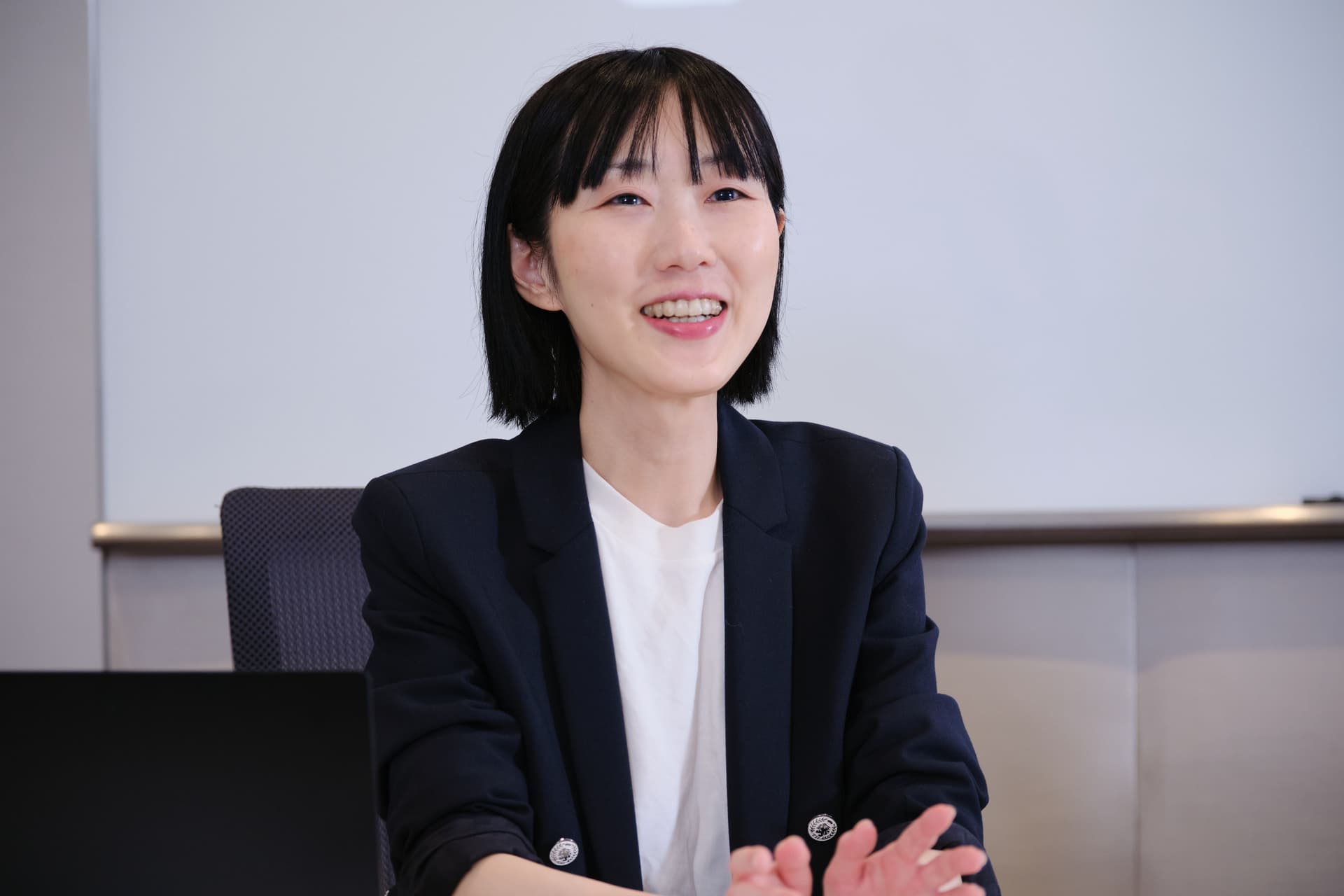 a woman in a suit and white shirt is sitting at a desk and smiling .