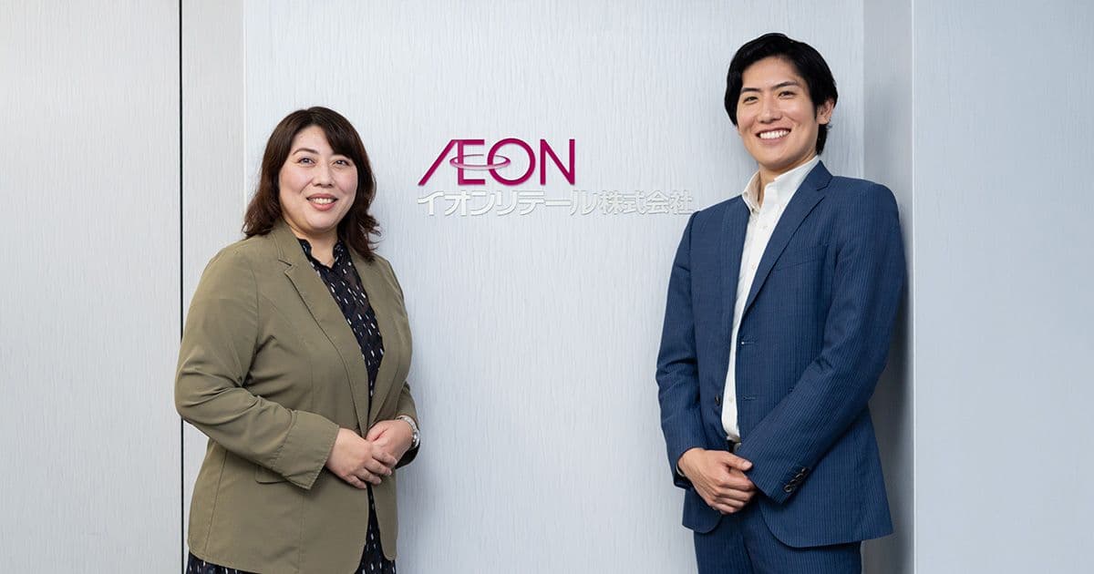 イオンのロゴの前に立つ笑顔の女性と男性。