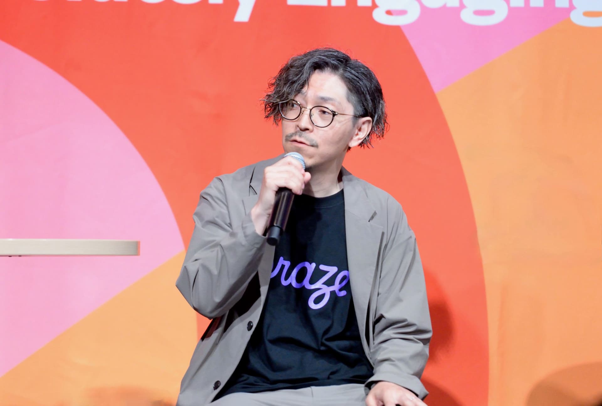 a man in a suit and glasses is sitting in front of a microphone .