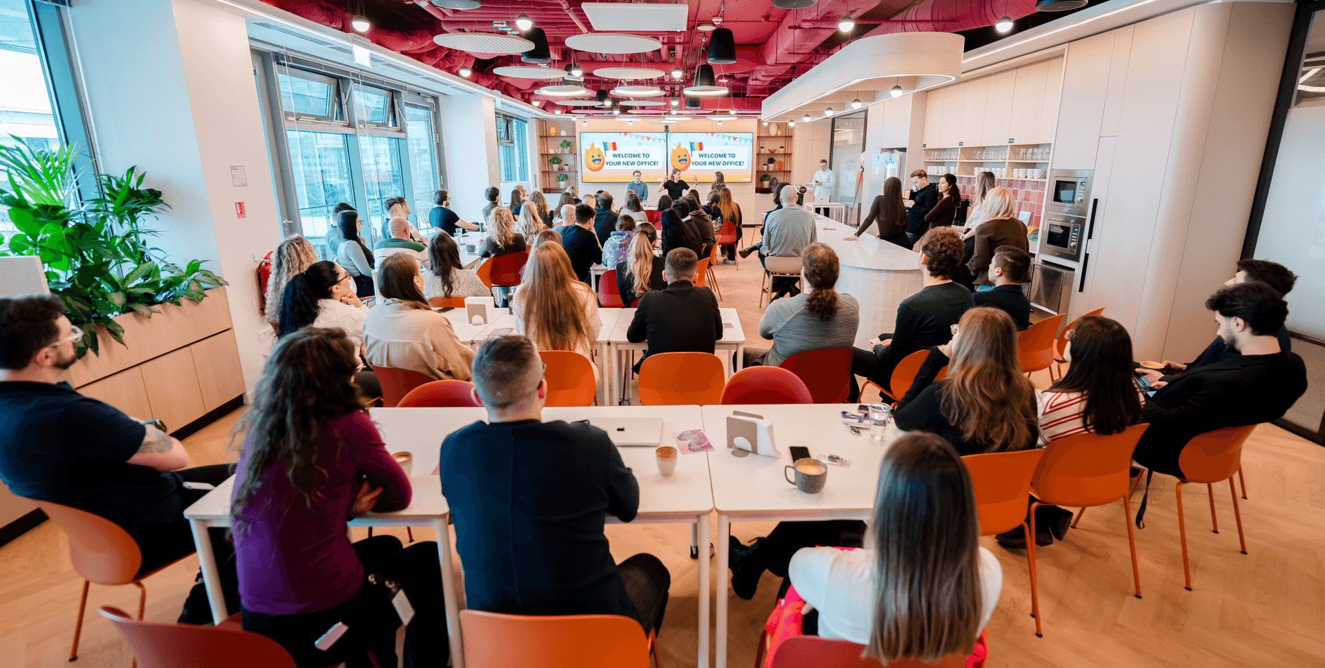 A group of people seated in a modern office space, facing a screen with a presentation.