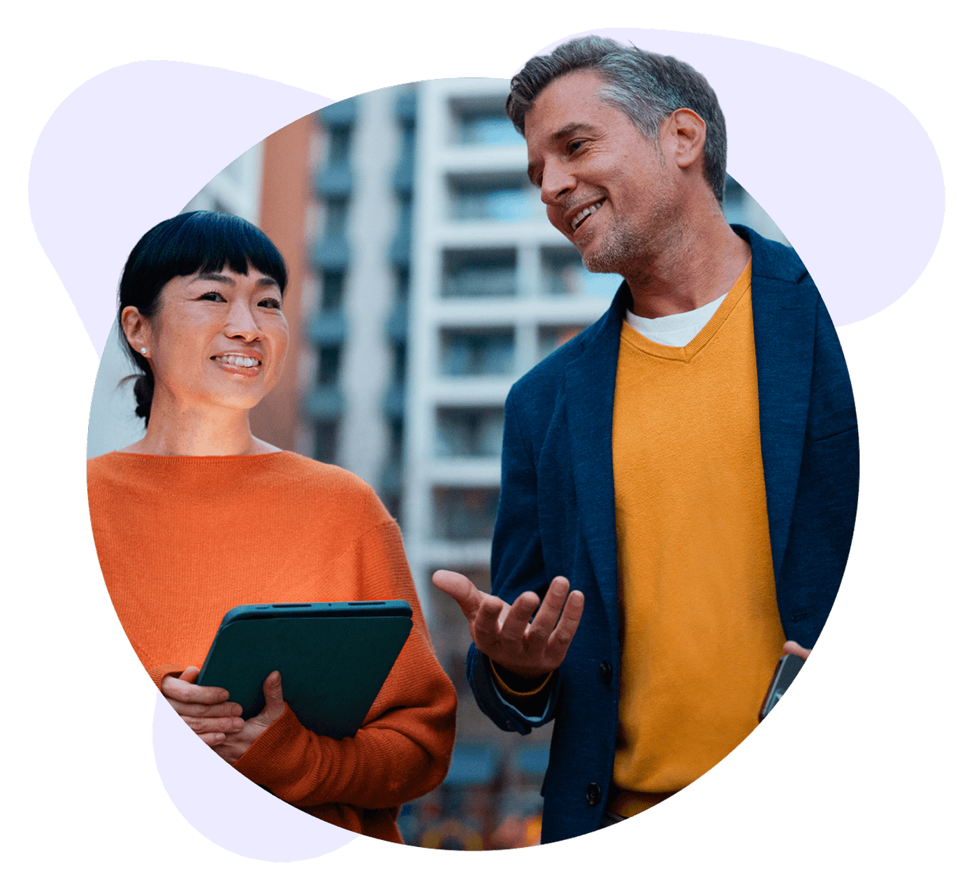 Smiling man and woman converse outdoors, the woman holding a tablet and the man gesturing.