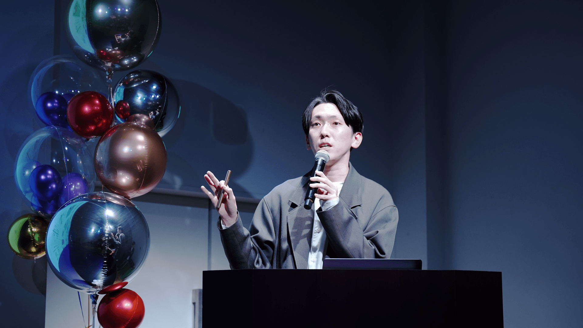 a man stands at a podium holding a microphone in front of balloons
