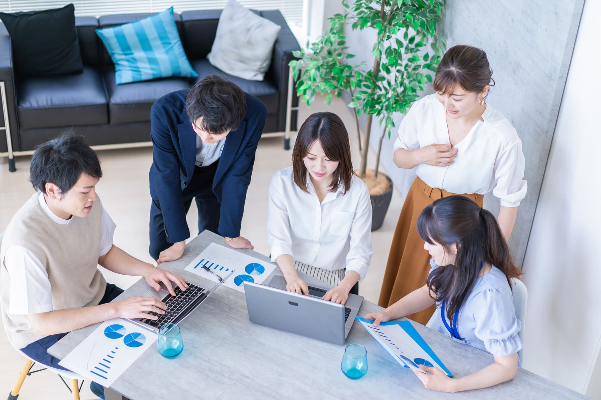 Five colleagues collaborating around a table with laptops and charts.