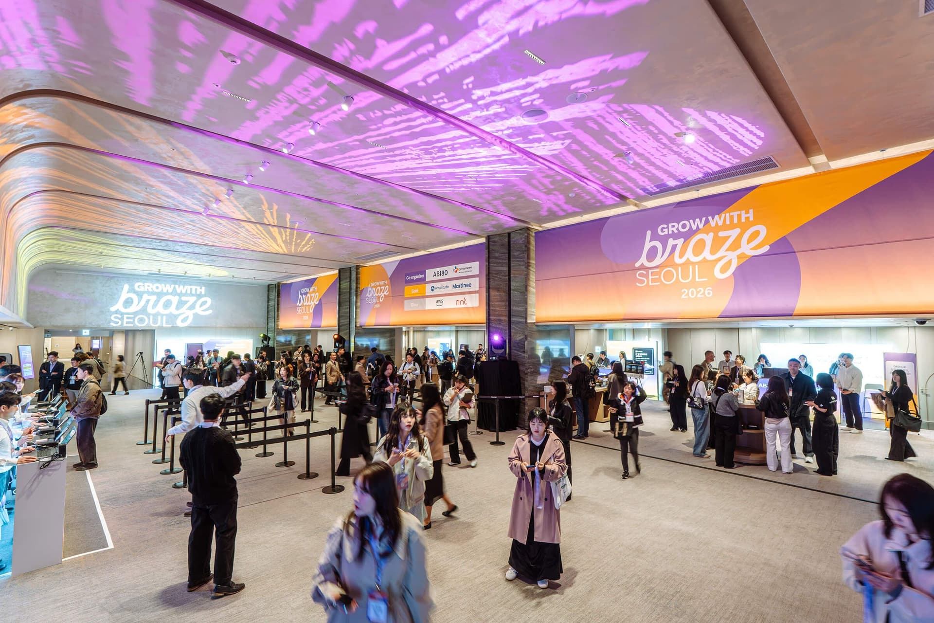Attendees mingle in a modern event hall under purple lighting, with large "Grow with Braze Seoul 2026" banners visible.