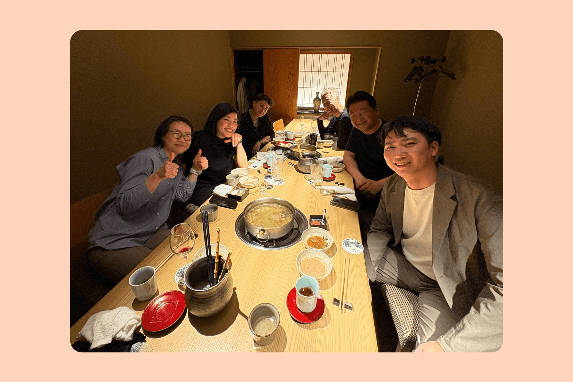 A group of seven people smiling and giving thumbs up while sitting around a table with a hot pot at a restaurant.