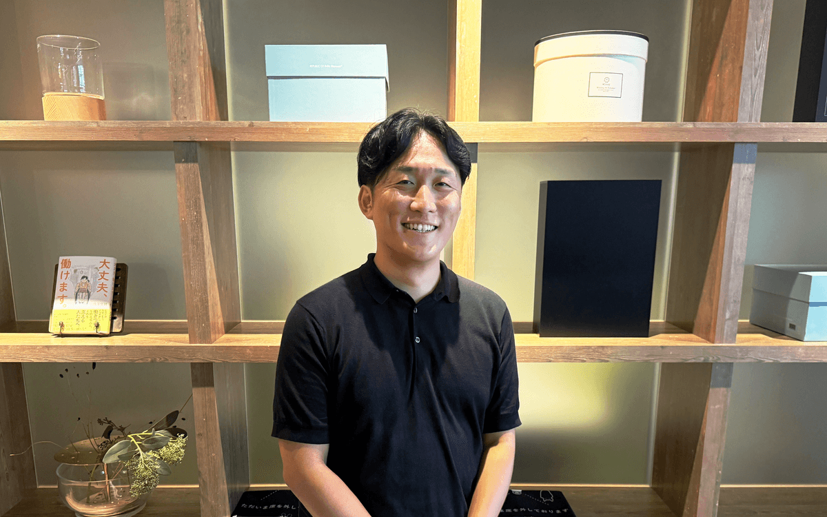 a man in a black shirt smiles in front of a bookshelf