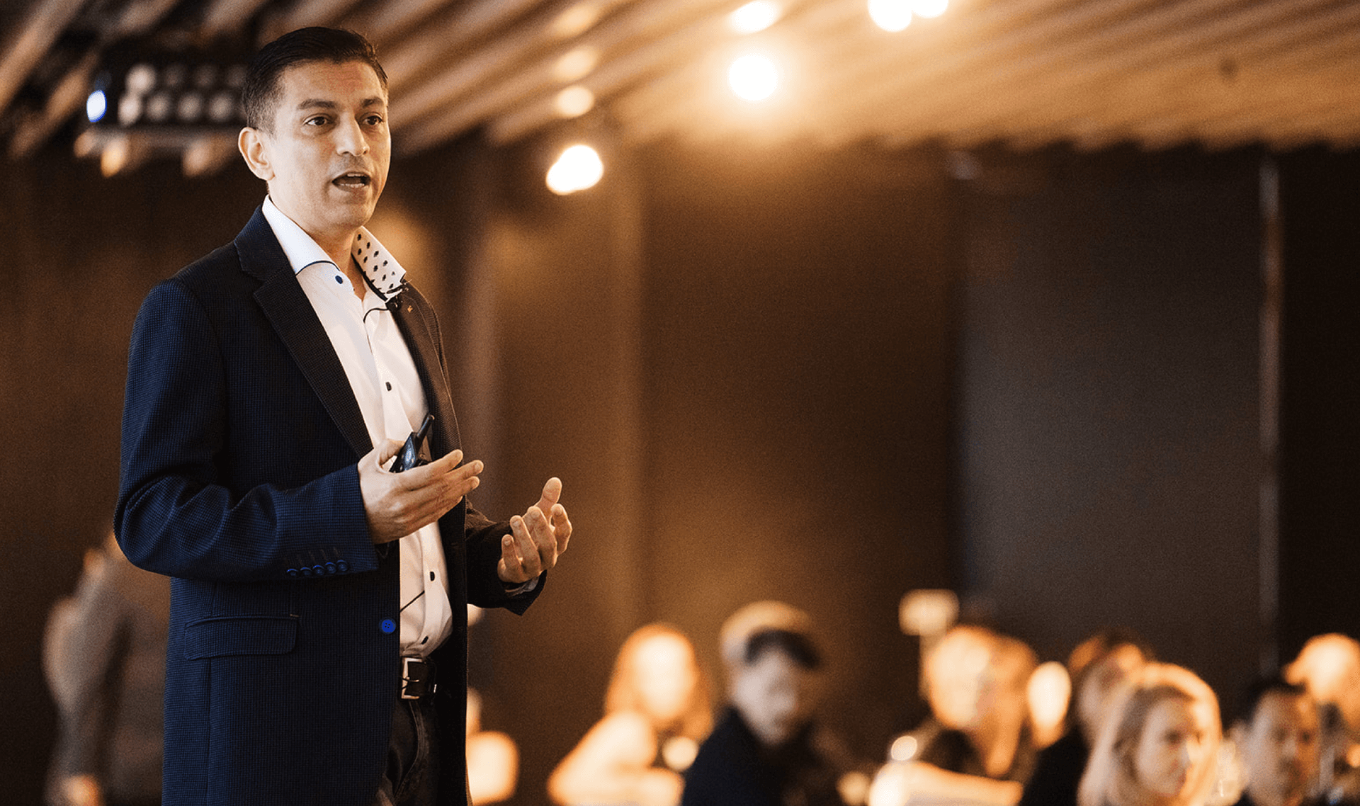 Man in a suit jacket speaking and gesturing to an audience.