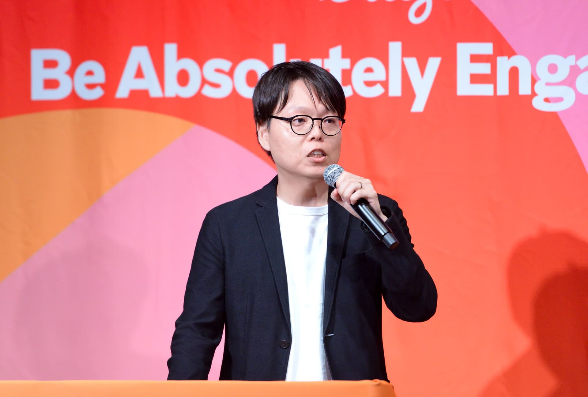 a man in a suit and glasses is standing at a podium holding a microphone .