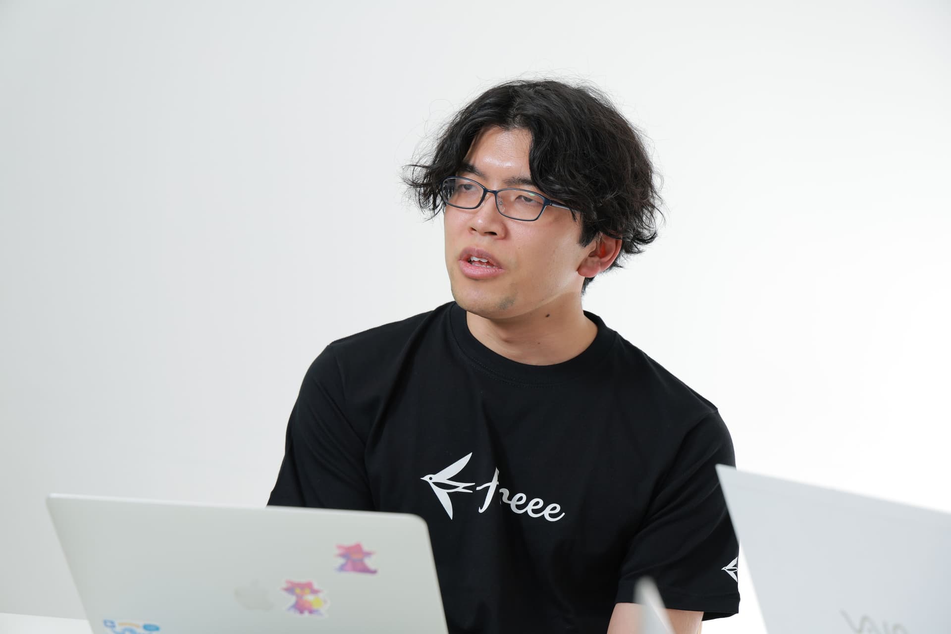 ビジネス基盤本部 IT企画推進部 MOps基盤チーム 萬田氏がPCの前でインタビューを受け、freeeのロゴ黒Tシャツを着ている