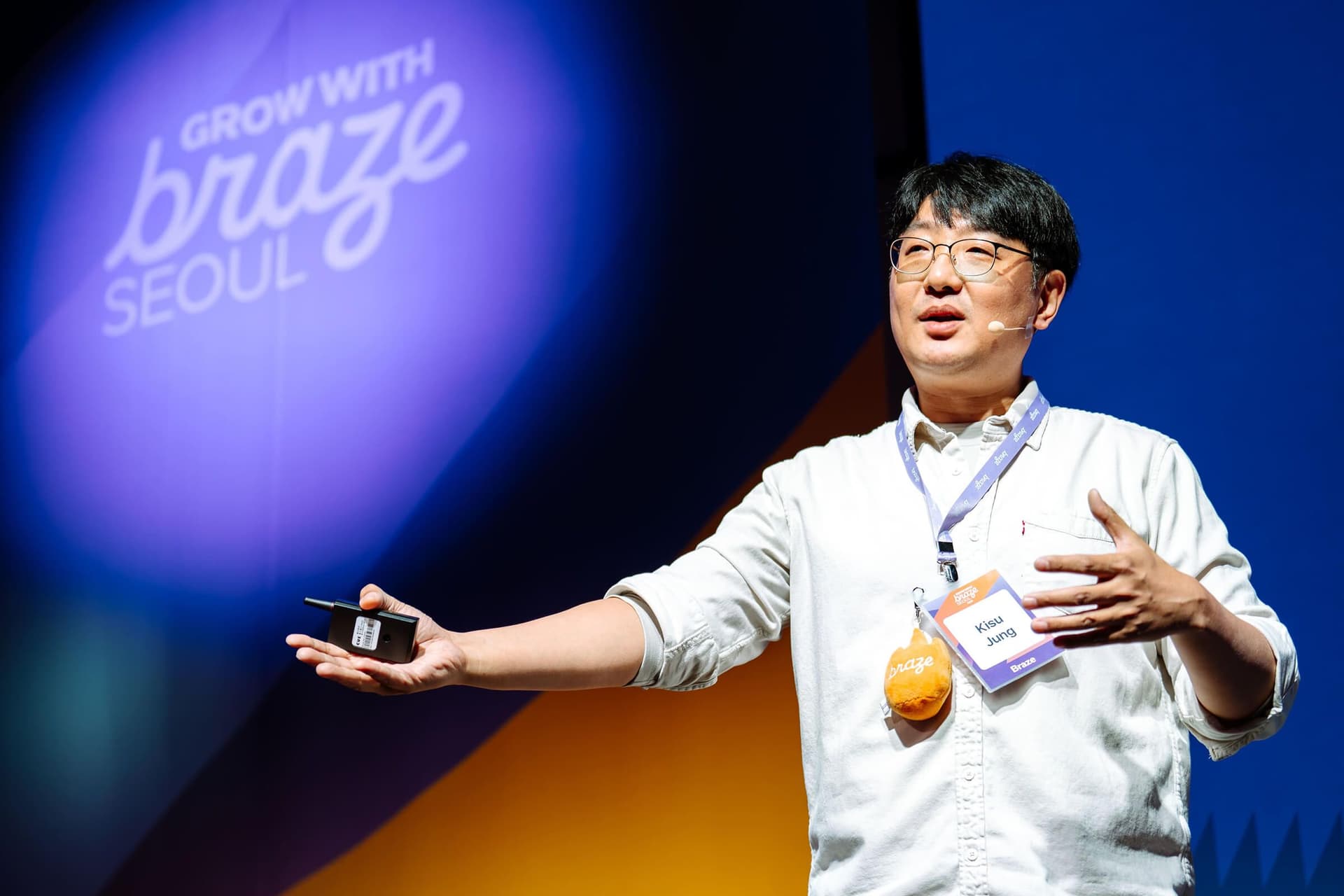 Kleo Jung speaking on stage at a Braze event, holding a device, with "Grow with Braze Seoul" projected behind him.