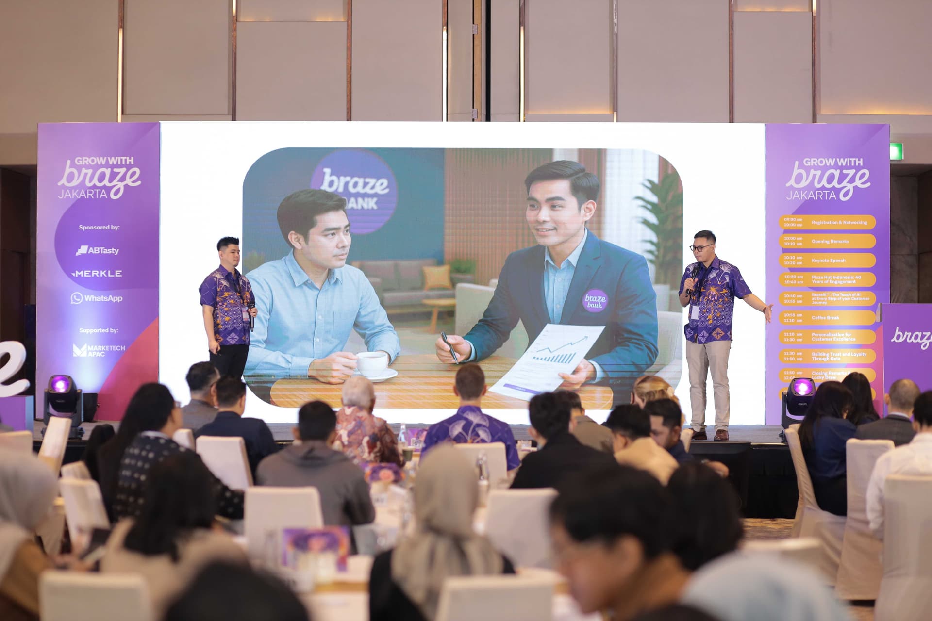 a group of people are sitting at tables in front of a large screen .