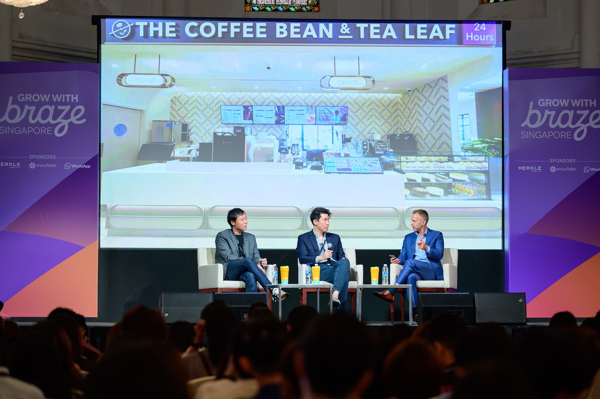 three men are sitting in front of a large screen at a conference .