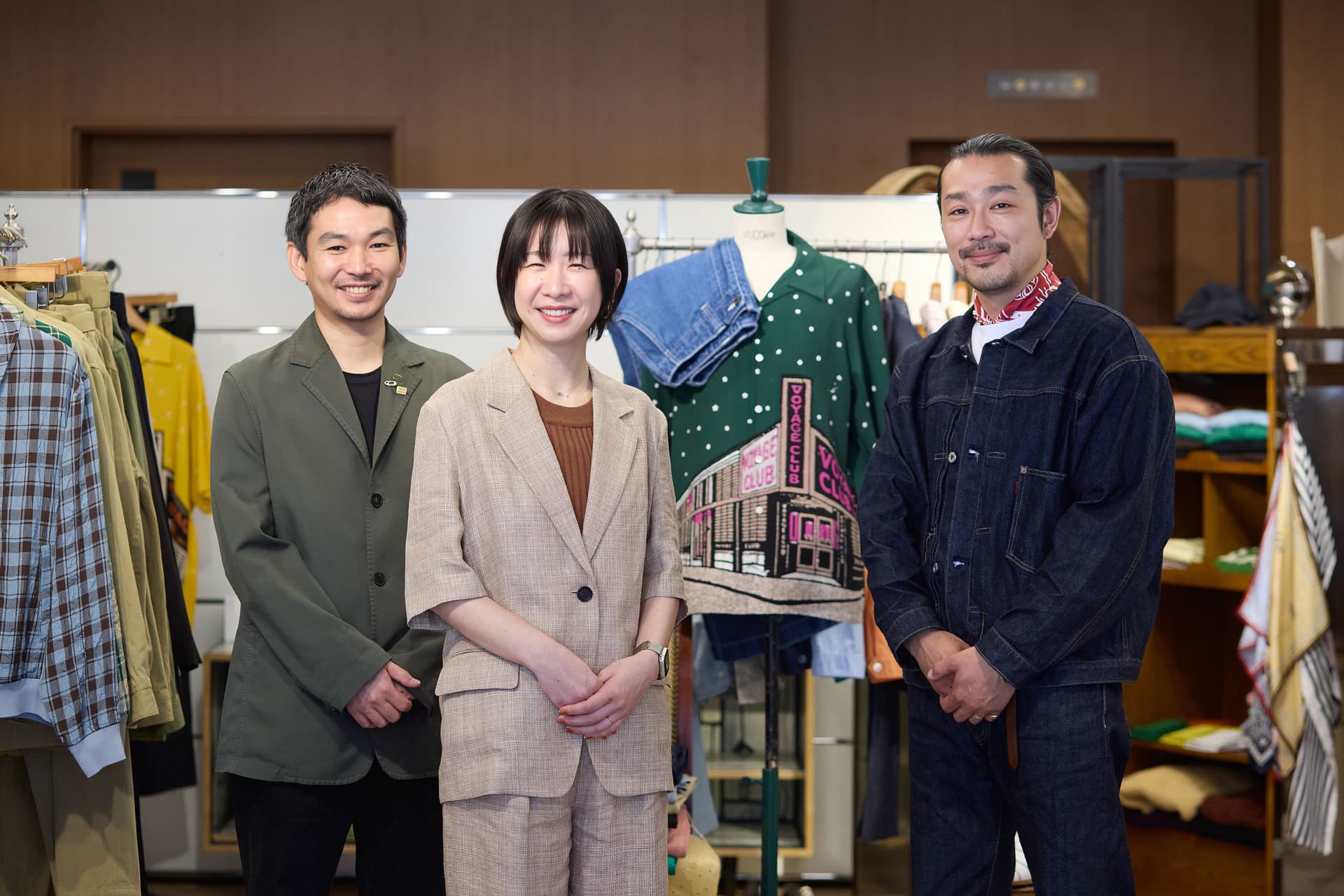 男性2人と女性1人の、笑顔の3人が、マネキンが置かれた衣料品店の中に立っている。