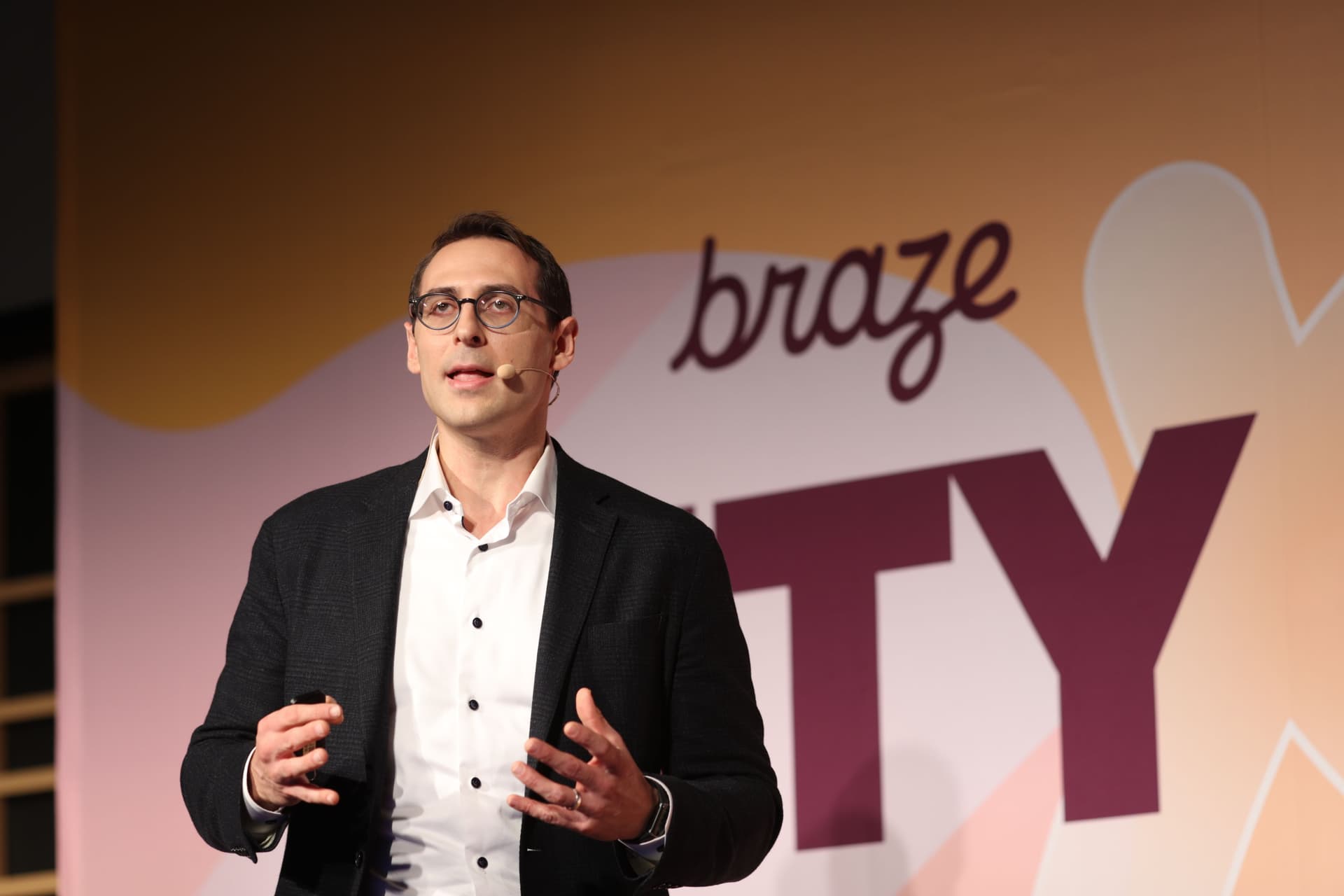 a man in a suit and glasses is giving a speech on a stage .