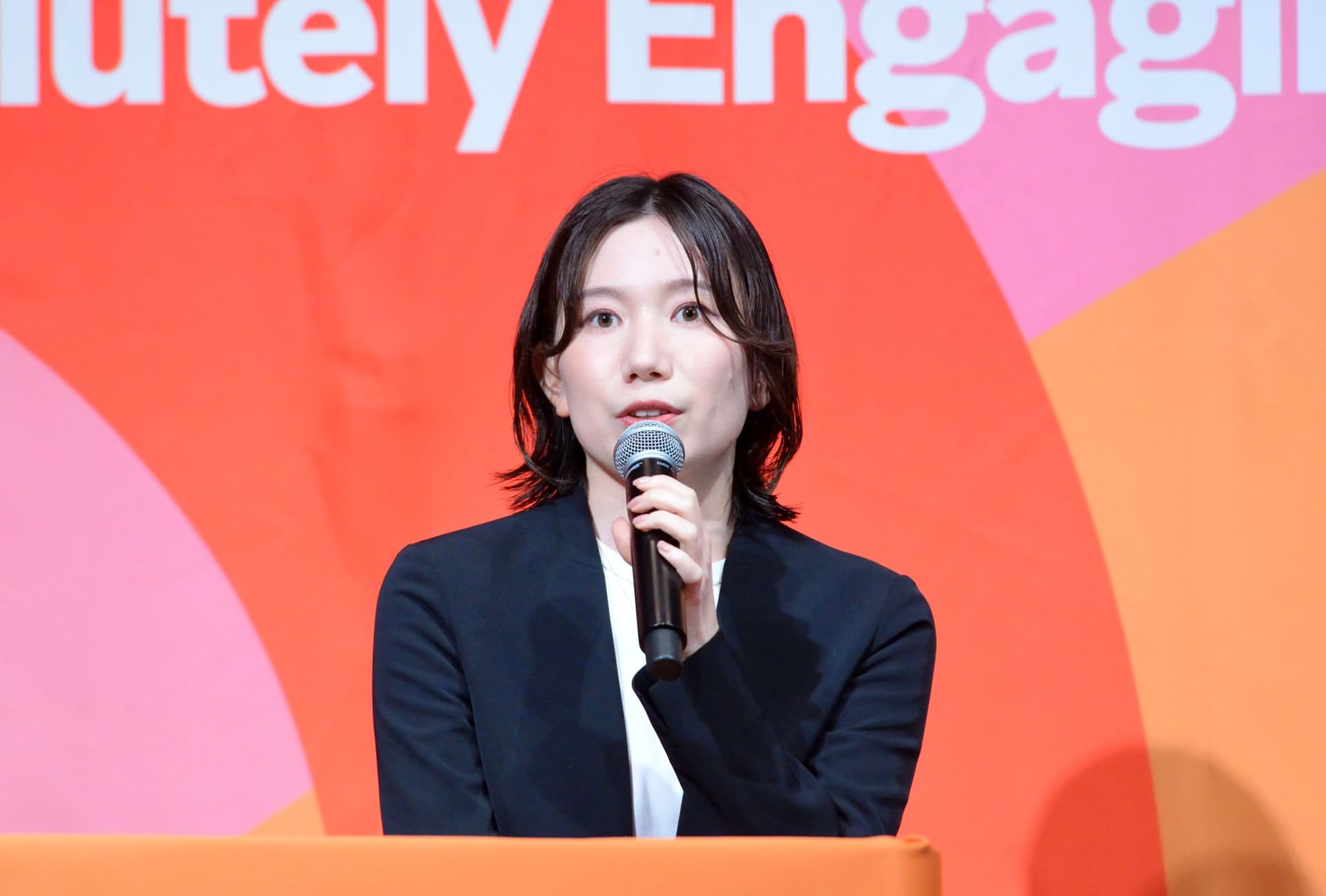 a woman in a suit is holding a microphone in front of a red background .