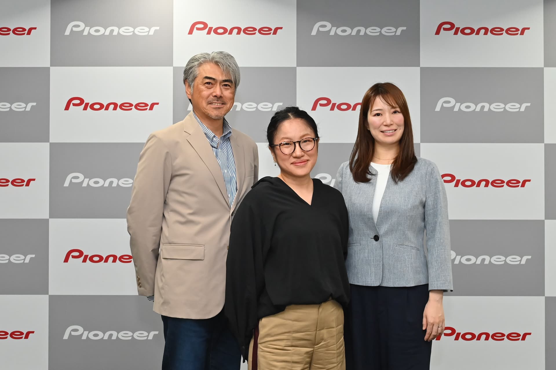 a man and two women are posing for a picture in front of a wall with pioneer written on it .