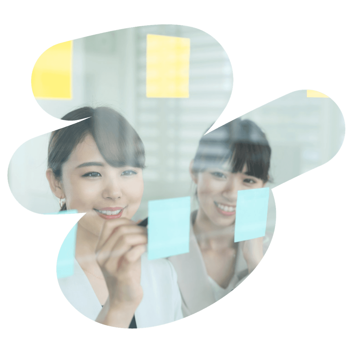 Two smiling women brainstorming with sticky notes on a clear glass board.