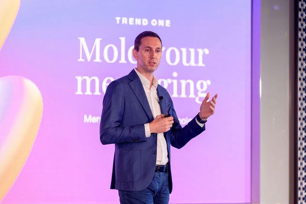 A man in a blue suit presents on stage with "Mold your messaging" displayed on a purple screen behind him.
