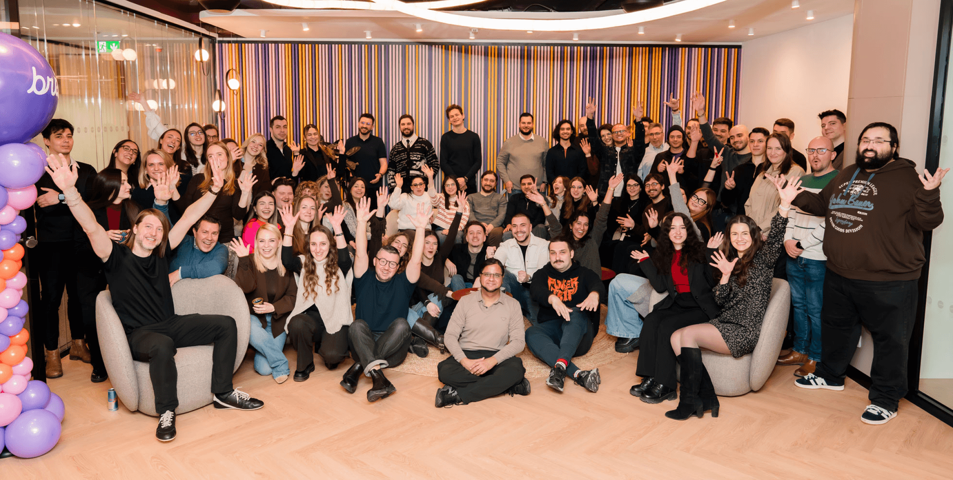 A large group of smiling people waving and posing for a photo in a modern office.