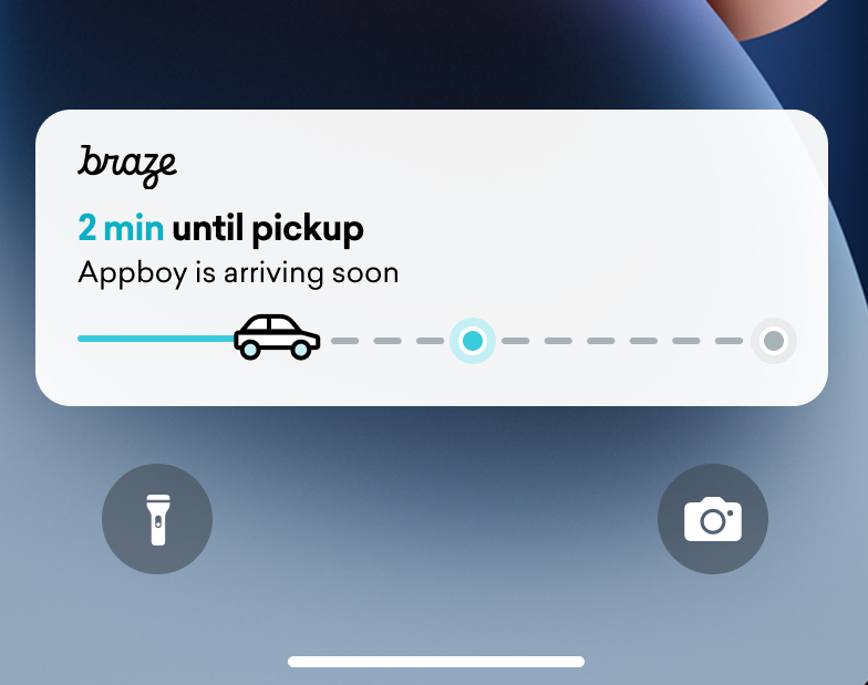 A delivery tracker live activity on an iPhone lockscreen. A status bar with a car is almost half-way filled up. Text reads "2 min until pickup"
