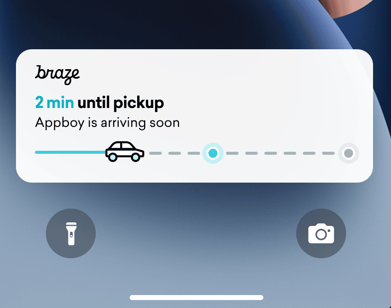 Live-Aktivität mit Zustellungs-Tracker auf dem Sperrbildschirm eines iPhones. Eine Statusleiste mit einem Auto ist fast zur Hälfte gefüllt. Der Text lautet „2 min until pickup“.